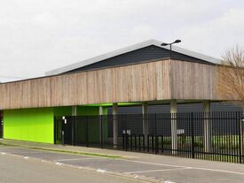 extérieur extension du complexe sportif en bardage bois et couleur vert avec vue sur parking depuis la rue des écoles.