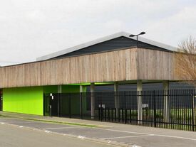 extérieur extension du complexe sportif en bardage bois et couleur vert avec vue sur parking depuis la rue des écoles.
