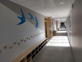 couloir de l'école avec décor d'oiseaux bleus et des casiers en bois pour ranger les chaussures.